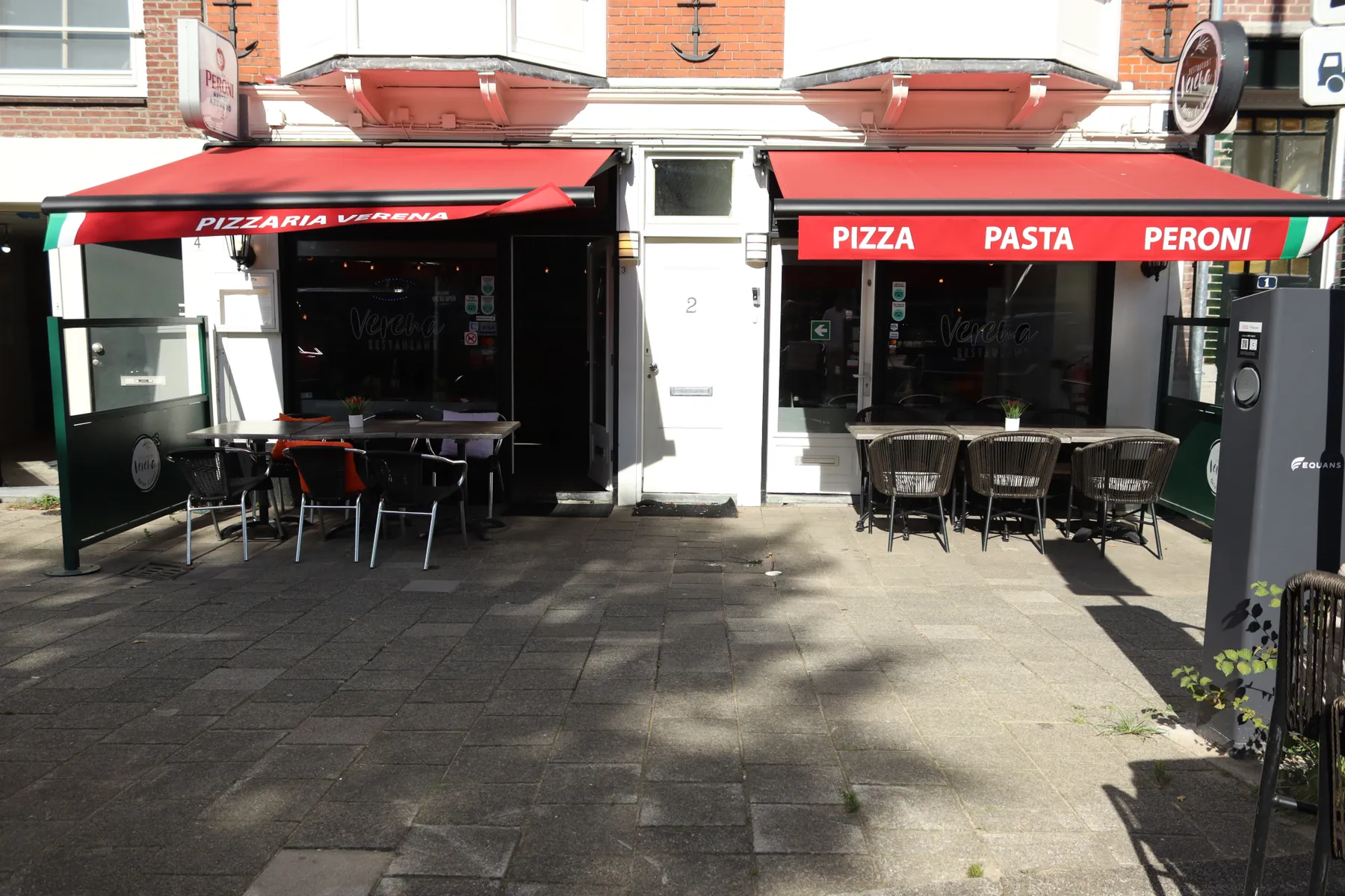 De gevel aan het Rapenburgerplein, met rode zonneschermen en het terras in de zon