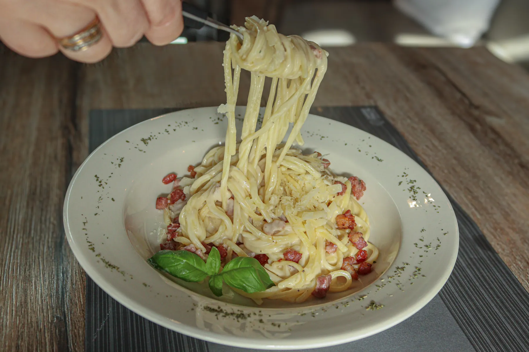 Een vork draait spaghetti carbonara op uit een bord, met basilicum erop